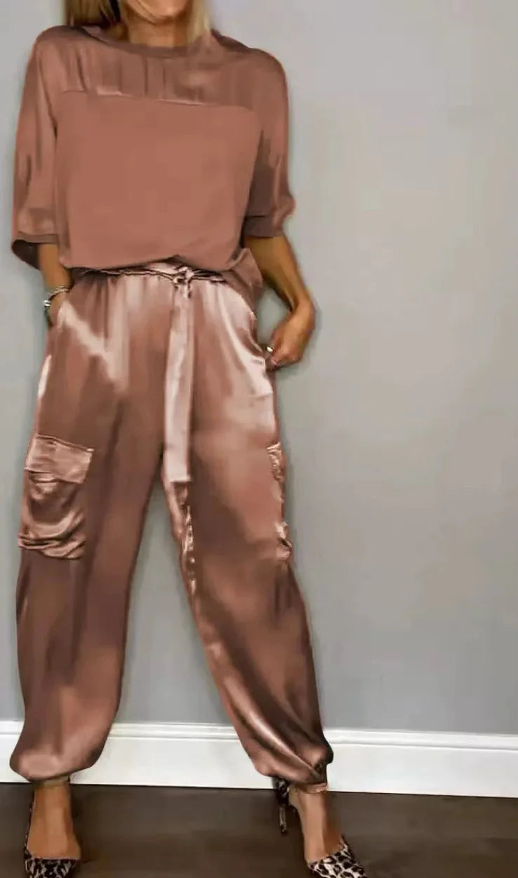 Brown outfit with sheer top and satin pants against a gray wall.