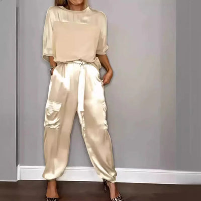 Person wearing a beige satin outfit against a gray wall